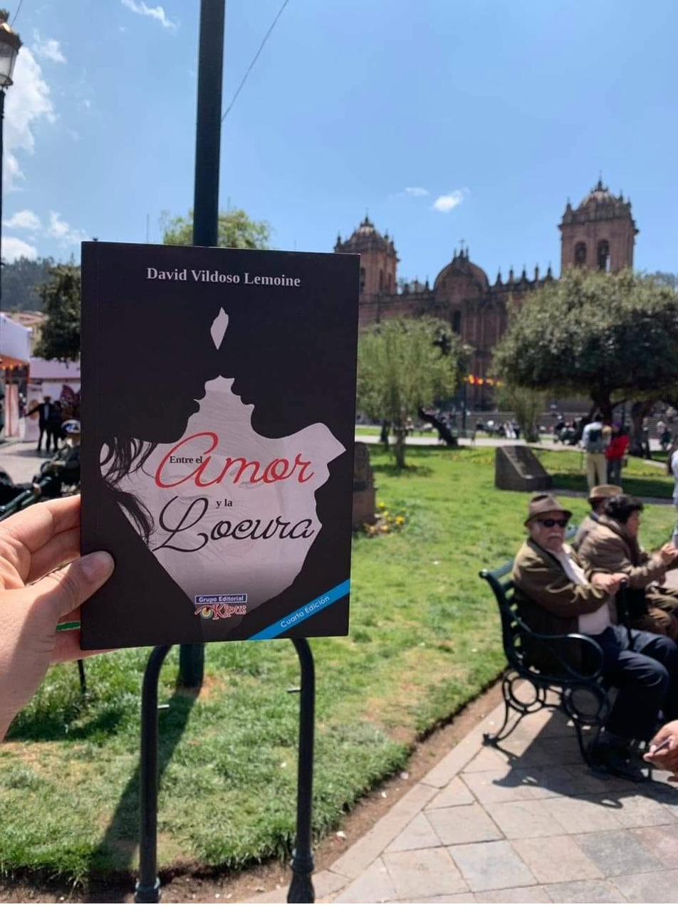 El libro Entre el Amor y la Locura de David Vildoso Lemoine frente a una iglesia colonial en Cusco, Perú